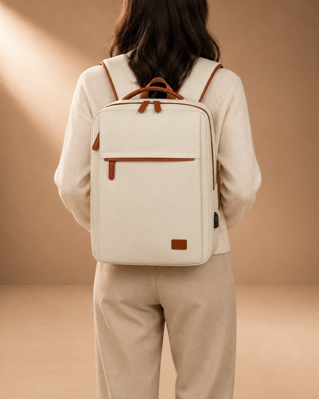 Off-white travel backpack worn on both shoulders, showing the front zipped pocket, tan handles and adjustable straps.
