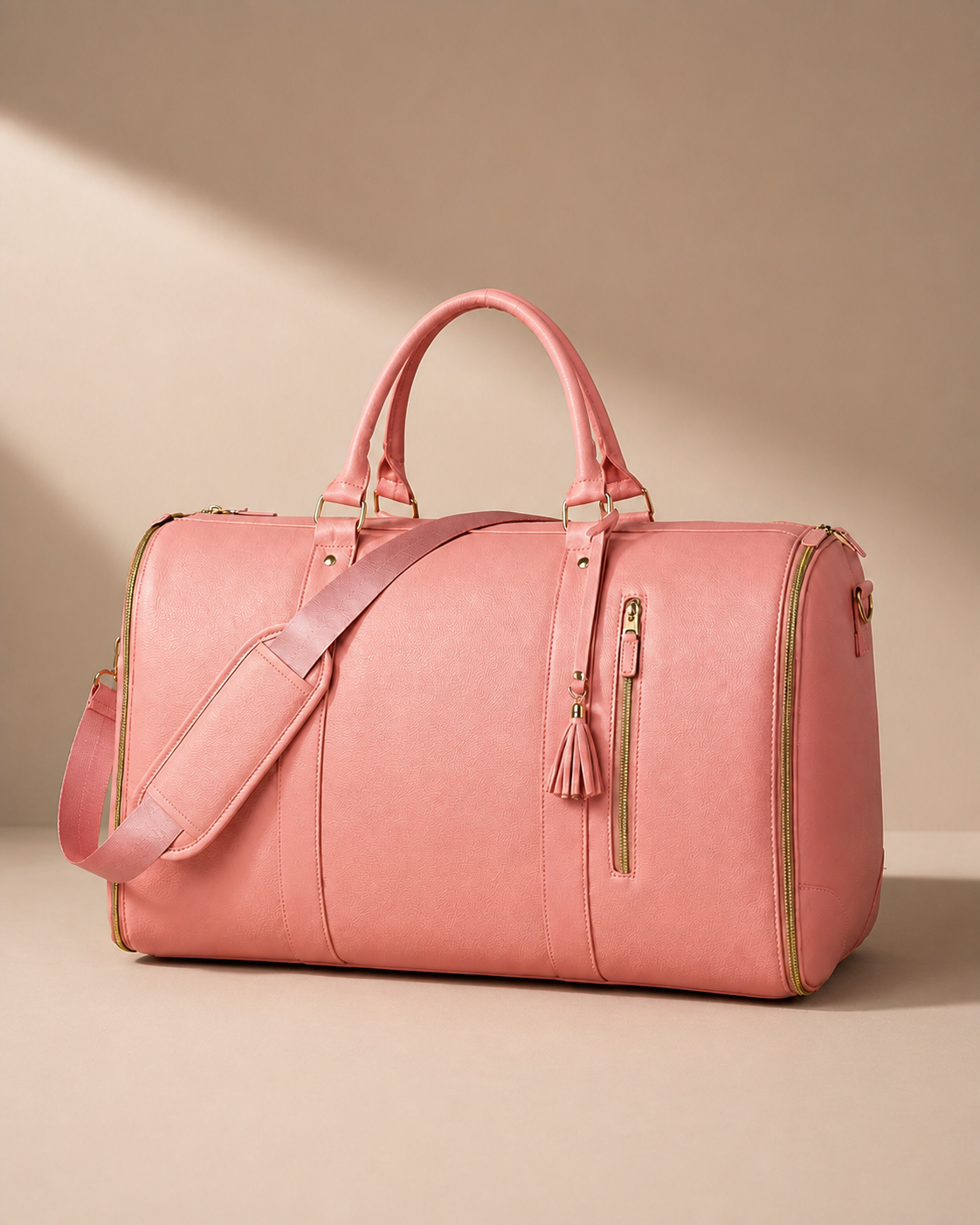 Pink garment travel bag with shoulder strap on a warm studio background